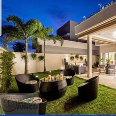 an outdoor living area with chairs and tables in the grass at night, surrounded by palm trees