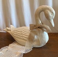 a white swan with a bow on its neck sitting on a table next to a doily