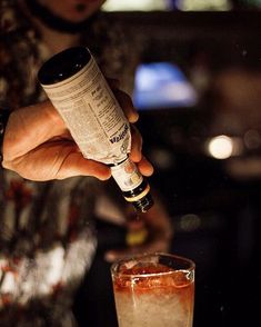 a person pouring something into a glass with a bottle in it and another drink next to it