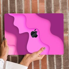 a person holding an apple logo in front of a pink and purple design on a brick wall