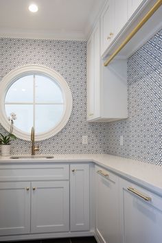 a kitchen with white cabinets and blue patterned wallpaper on the walls, along with a round window