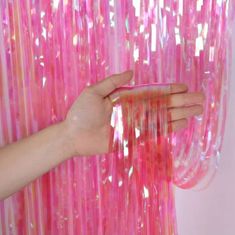 a hand is reaching for pink streamers hanging from a white wall in front of a woman's hand