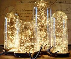 three glass bottles with lights in them on top of a wooden table next to antlers