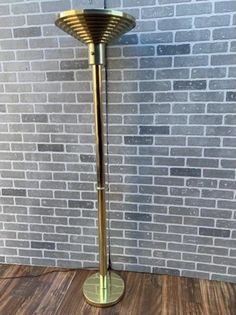 a gold colored floor lamp on a wood floor in front of a brick wall and wooden floor