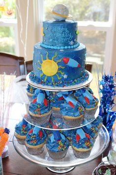 a three tiered cake and cupcakes on a table