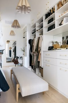 a white closet with lots of clothes hanging on the shelves and shoes sitting on top of it