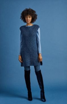 a woman standing in front of a blue background wearing black boots and a sweater dress