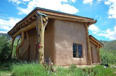 a small adobe building sitting on top of a lush green field