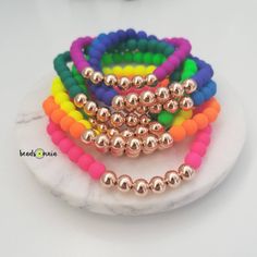 four different colored bracelets on a white marble plate with pink, yellow, green, orange and blue beads