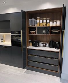 a kitchen with black cabinets and white tile flooring is shown in this image, there are many items on the shelves