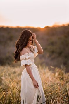 a woman in a white dress is standing in tall grass and looking off into the distance