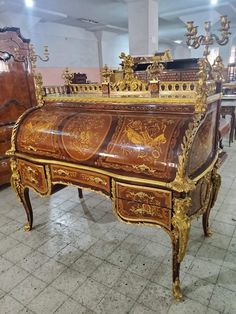 an ornately decorated desk with gold trimmings in a room filled with wooden furniture