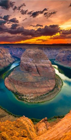 the river is surrounded by large rocks and green water under a cloudy sky at sunset