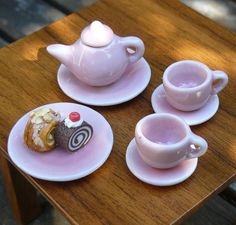 three tea cups and saucers with pastries on them sitting on a wooden table