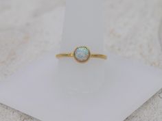 This stunning minimalistic ring features a lab created white opal set in a delicate yellow gold filled bezel setting. The band is the perfect balance of minimalist and durable. The dainty ring looks gorgeous by itself or stacked with other rings! Setting Details- Material: 14/20 Yellow Gold Filled Band Width: 1.7mm Gemstone Details- Gemstone: Opal Type: Lab Created Color: White Size: 6mm Shape: Round As with any gemstone, there can be some variation in color and tone. The ring ships in a custom Minimalist Opal Ring With Bezel Setting As Gift, Minimalist Gold Opal Ring As Birthstone, Minimalist Opal Birthstone Ring, Gold Stackable Opal Ring, Gold Opal Stackable Ring, Gold Adjustable Opal Ring, Round Shape, Gold Opal Ring Adjustable, Adjustable Gold Opal Ring, Minimalist Opal Stackable Promise Rings