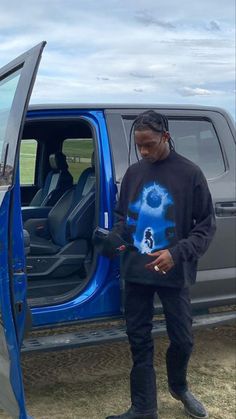 a man standing in the open door of a blue truck with his hands on his hip