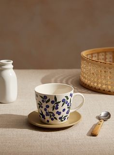 a cup and saucer sitting on a table next to a basket with spoons