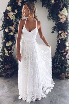 a woman wearing a white dress standing in front of a floral arch