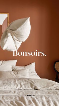 a bed with white sheets and pillows in front of an orange wall that says bonsors