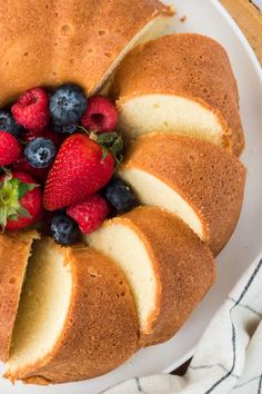 a bundt cake with sliced strawberries and blueberries in the middle on a white plate