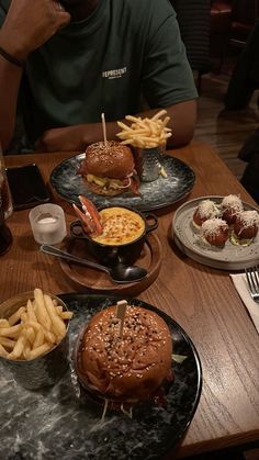 a man sitting at a table with plates of food on it and french fries in front of him