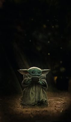 a baby yoda holding a cell phone in the dark