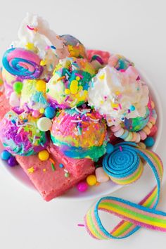 a white plate topped with cake covered in candy and sprinkles next to a rainbow lollipop