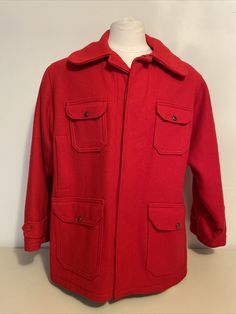 An MCM classic. Stand-out red wool in a classic longer ("car-coat") design with 8 pockets for the handy outdoorsman or woman. Button-front coat has a tan flannel lining with 6 front pockets (four with vintage logo buttons and two slip-in) plus two buttoned pockets in the side backs. Wrists have elasticized inner cuffs and outer flaps are adjustable by buttons to tighten against the weather. Label reads Woolrich Woolen Mills established 1830 Woolrich, Pa. 511 Size 46; fraying label still reads 10 Classic Solid Utility Jacket With Welt Pockets, Vintage Utility Jacket With Lapel Collar And Patch Pockets, Vintage Utility Jacket With Lapel Collar And Welt Pockets, Classic Solid Sport Coat With Pockets, Vintage Winter Utility Jacket With Lapel Collar, Vintage Utility Jacket With Lapel Collar For Winter, Vintage Long Sleeve Outerwear With Multiple Pockets, Red Winter Outerwear With Welt Pockets, Solid Sport Coat With Pockets And Flat Front