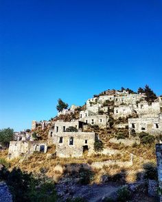 an old stone building sitting on top of a hill covered in grass and bushes under a blue sky