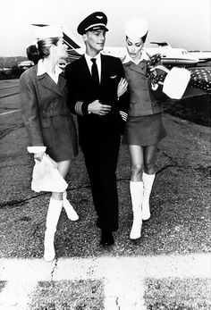 three women in flight uniforms are walking towards an airplane on the tarmac, with one woman holding her arm around the man's shoulder