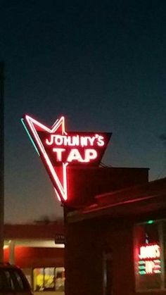 a neon sign that says johnny's tap on the side of a building at night