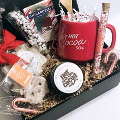 a red coffee mug surrounded by sweets and candies in a black gift box on a white surface