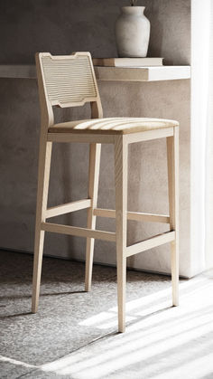 a wooden stool sitting next to a white vase on top of a table in front of a wall