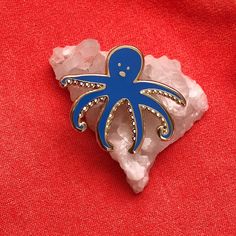 an octopus brooch sitting on top of a piece of white rock next to a red cloth