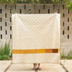 a person standing in front of a white and yellow quilted wall hanging on a fence