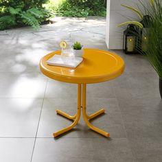 a yellow table sitting on top of a cement floor next to a potted plant