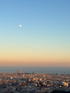 the moon is setting over an urban area with tall buildings and skyscrapers in the distance