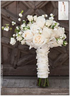 a bridal bouquet with white roses and greenery in front of a wooden door