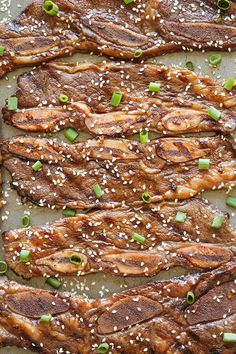 steak with sesame seeds and green onions on a baking sheet