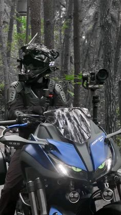 a man riding on the back of a blue and black motorcycle in front of trees