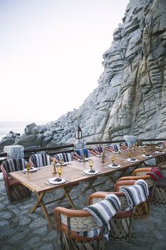 an outdoor dining area with wooden tables and chairs near the water's edge, next to a rocky cliff