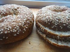 two bagels with sesame seeds sit on a cutting board next to a window sill