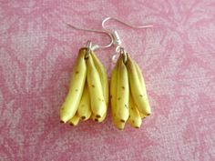 two pairs of bananas hanging from hooks on a pink tablecloth covered surface with white speckles