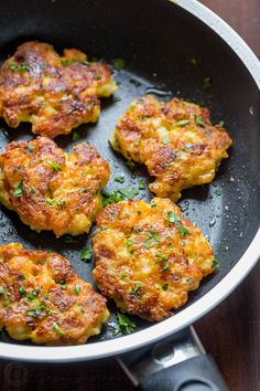 some crab cakes are cooking in a pan on the stove top with green garnishes