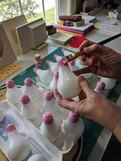 a person is painting plastic bottles with pink and white caps on them in front of a window