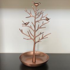 a metal tree with two birds on it sitting in a bowl next to a wall