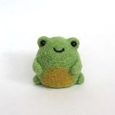 a small green stuffed frog sitting on top of a white surface with its eyes closed