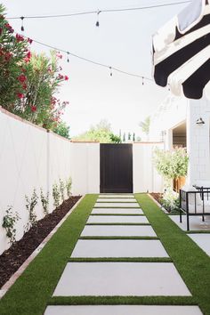 an outdoor patio area with grass and stepping stones on the ground, next to a white fence