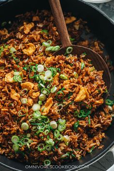 a skillet filled with fried rice and green onions, topped with wooden spoons