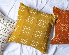 three decorative pillows on a bed with white sheets